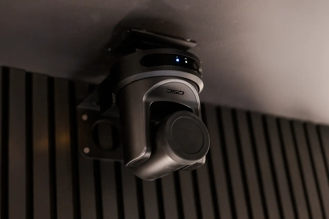 Ceiling-mounted pan-tilt-zoom security camera against a dark slatted wall